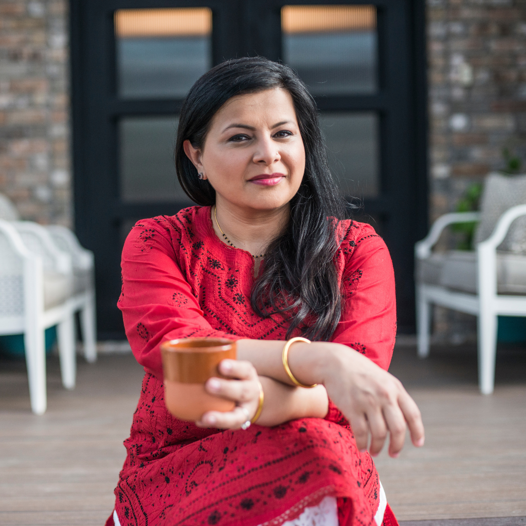 Woman in a red patterned dress holds a terracotta cup while wearing a gold bangle at a BuDhaGirl cookbook celebration event