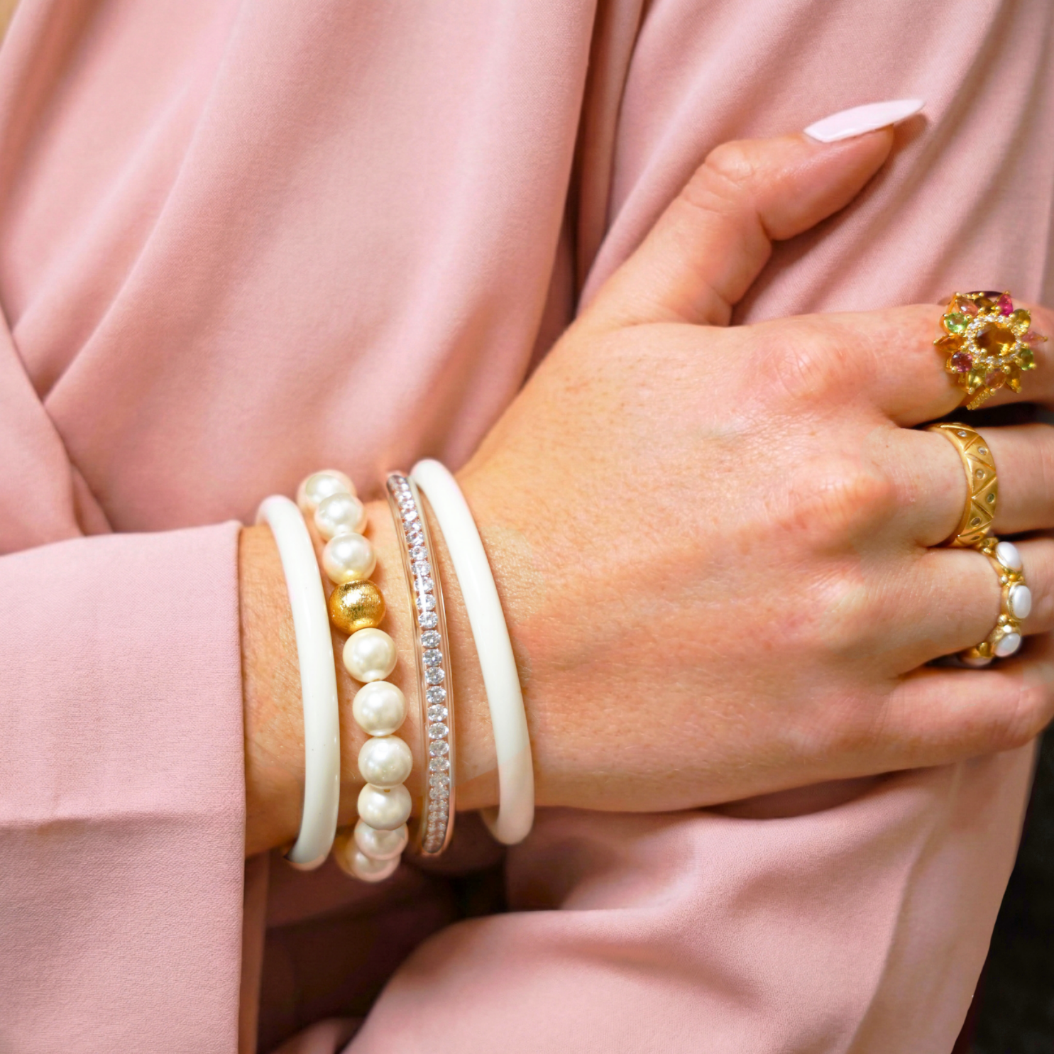 Close-up of a hand wearing multiple bracelets and rings on a maroon fabric background