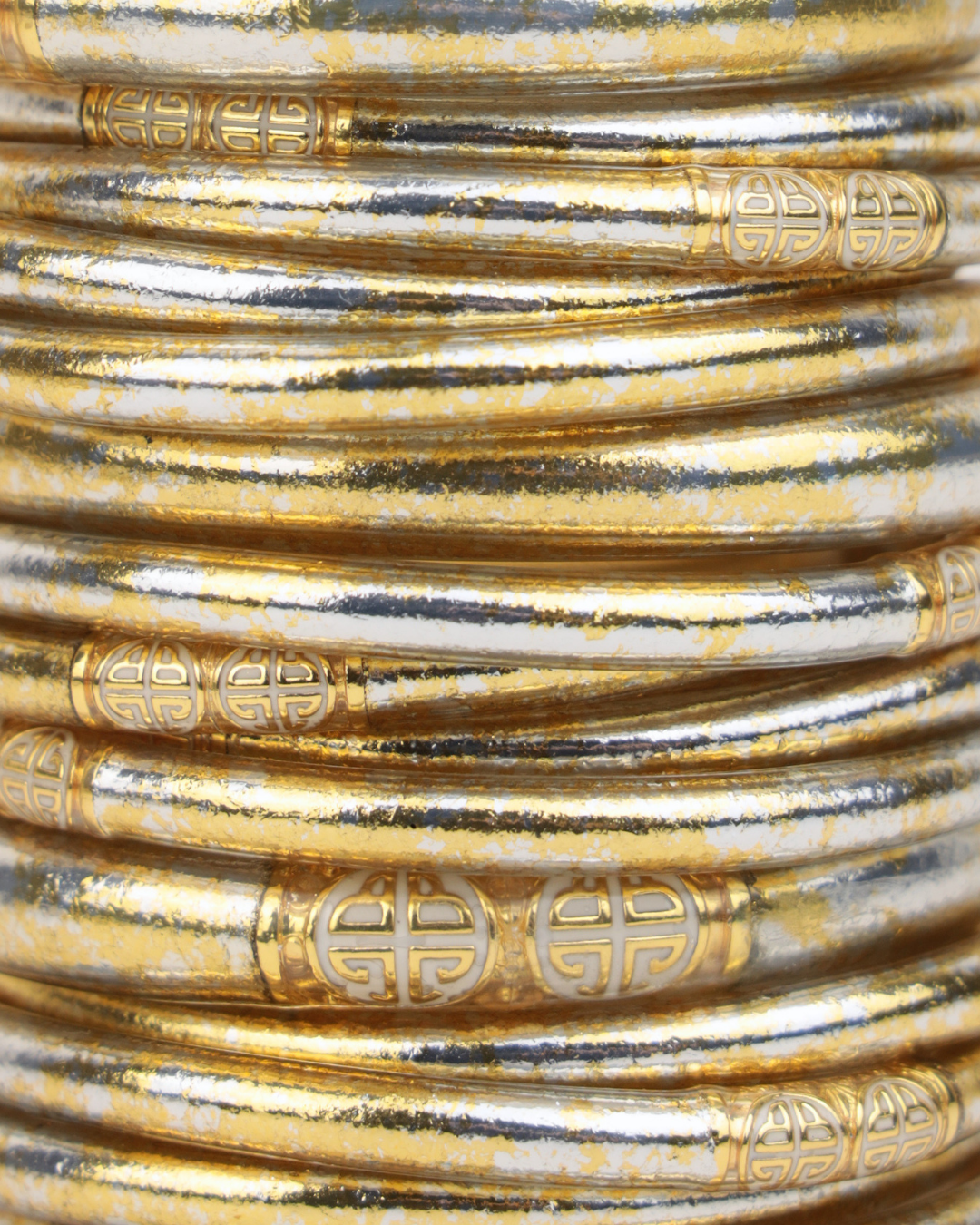 Close up of stacked gold and silver bangle bracelets with intricate engraved geometric accents and a distressed metallic finish