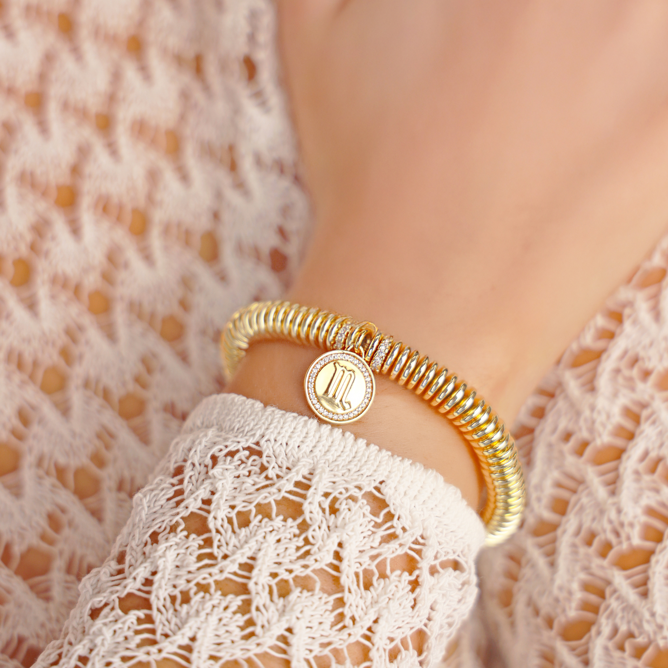 Gold bracelet with a circular charm on a person wearing a white lace garment.