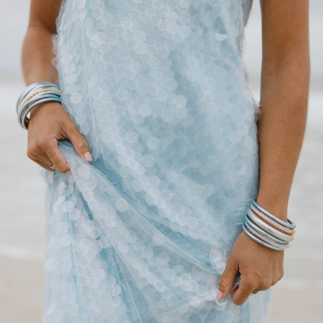 Close-up of a person wearing a light blue dress with floral patterns and multiple bracelets on a neutral background.