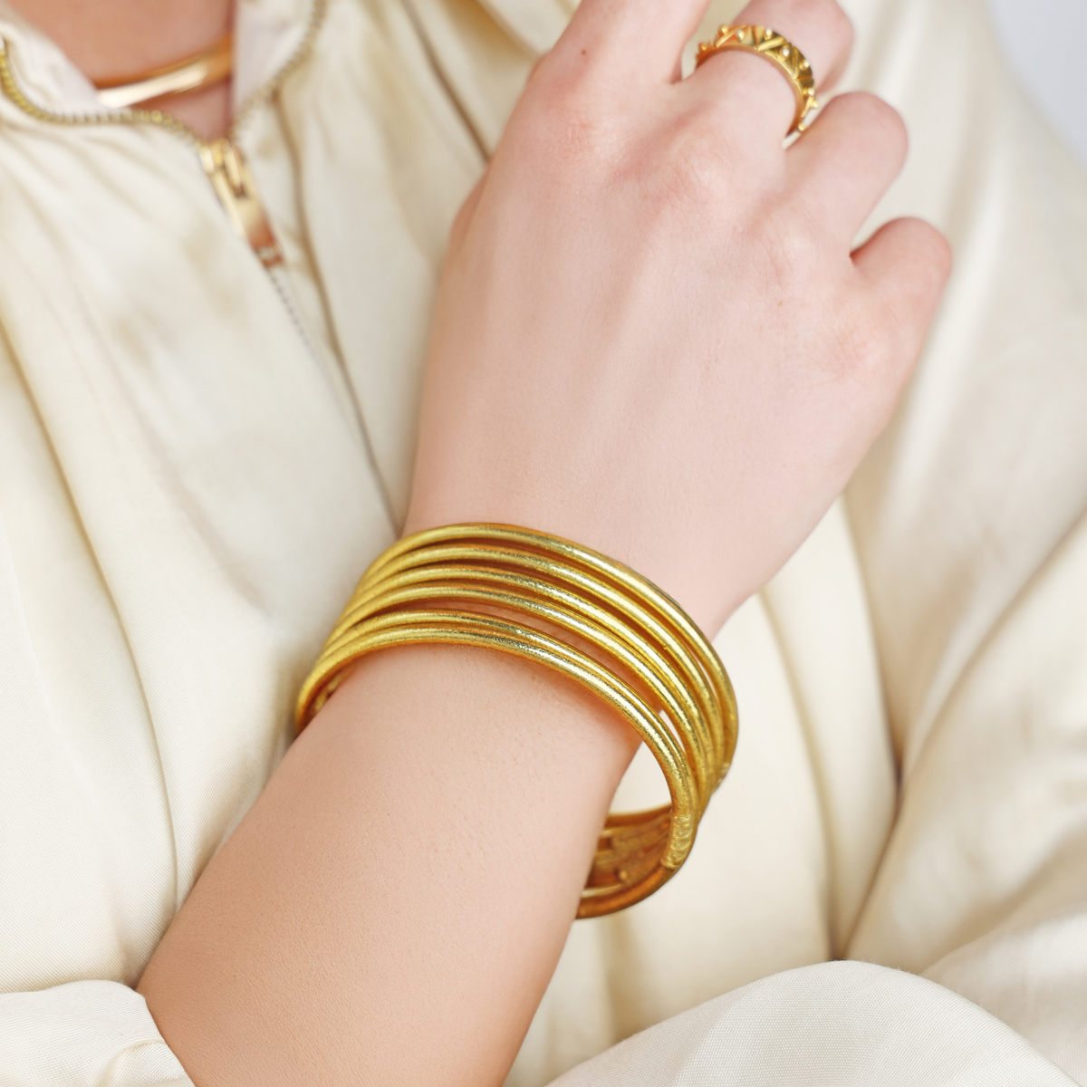 Gold bangles on a hand with a white fabric background