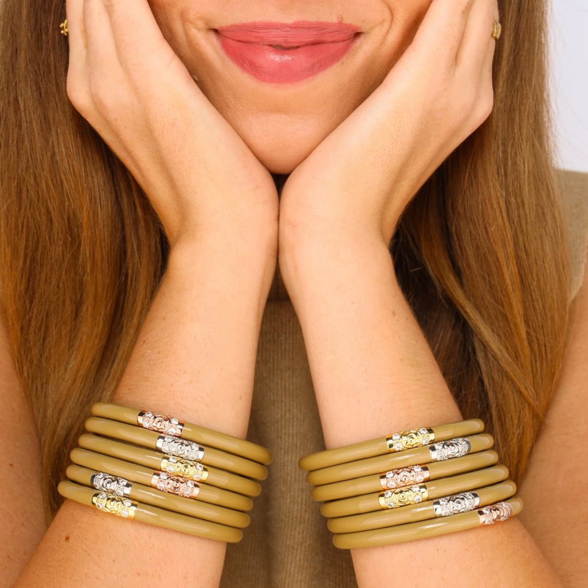 Woman wearing multiple bracelets on her wrists with a neutral background