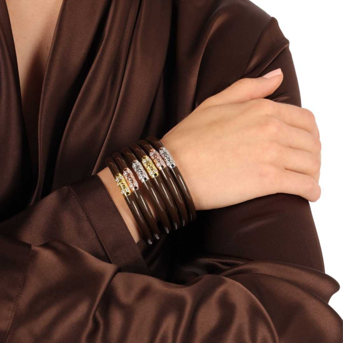Hand wearing multiple bracelets on a brown fabric background