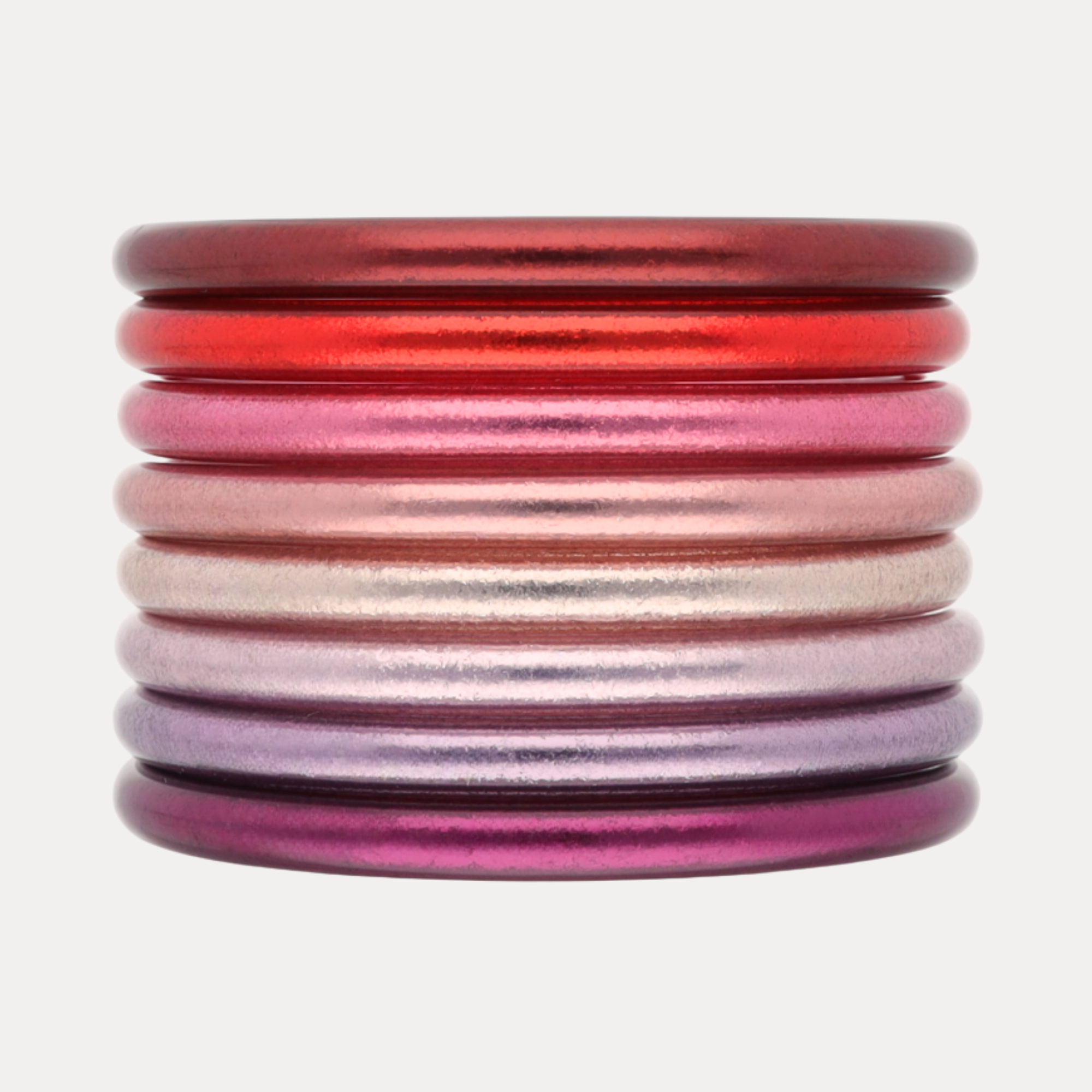 A stack of eight metallic bangles with a gradient color scheme transitioning from deep red at the top to pink, rose gold, champagne, lavender, and purple at the bottom, set against a plain light gray background.