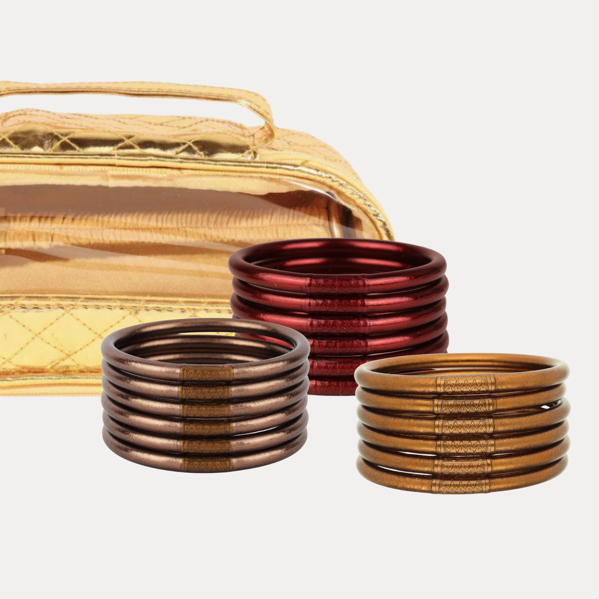 A bundle of bronze, brown, and red metallic All Weather Bangles with a gold travel case