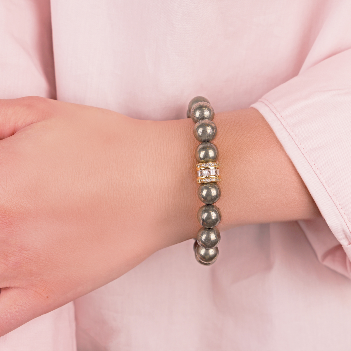 Bracelet with metallic beads on a wrist against a pink background