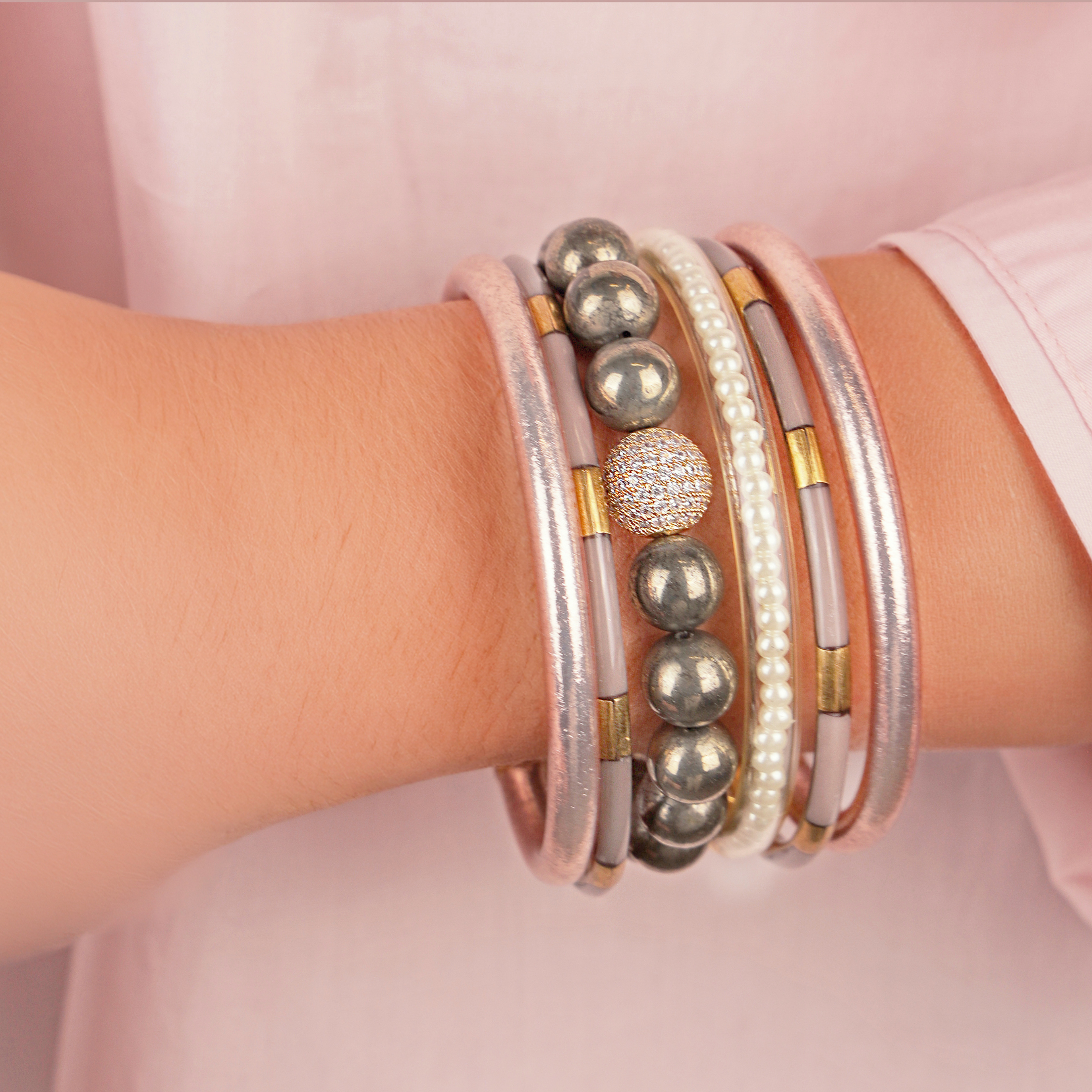 Close-up of a wrist wearing multiple bracelets with beads and pearls on a pink background