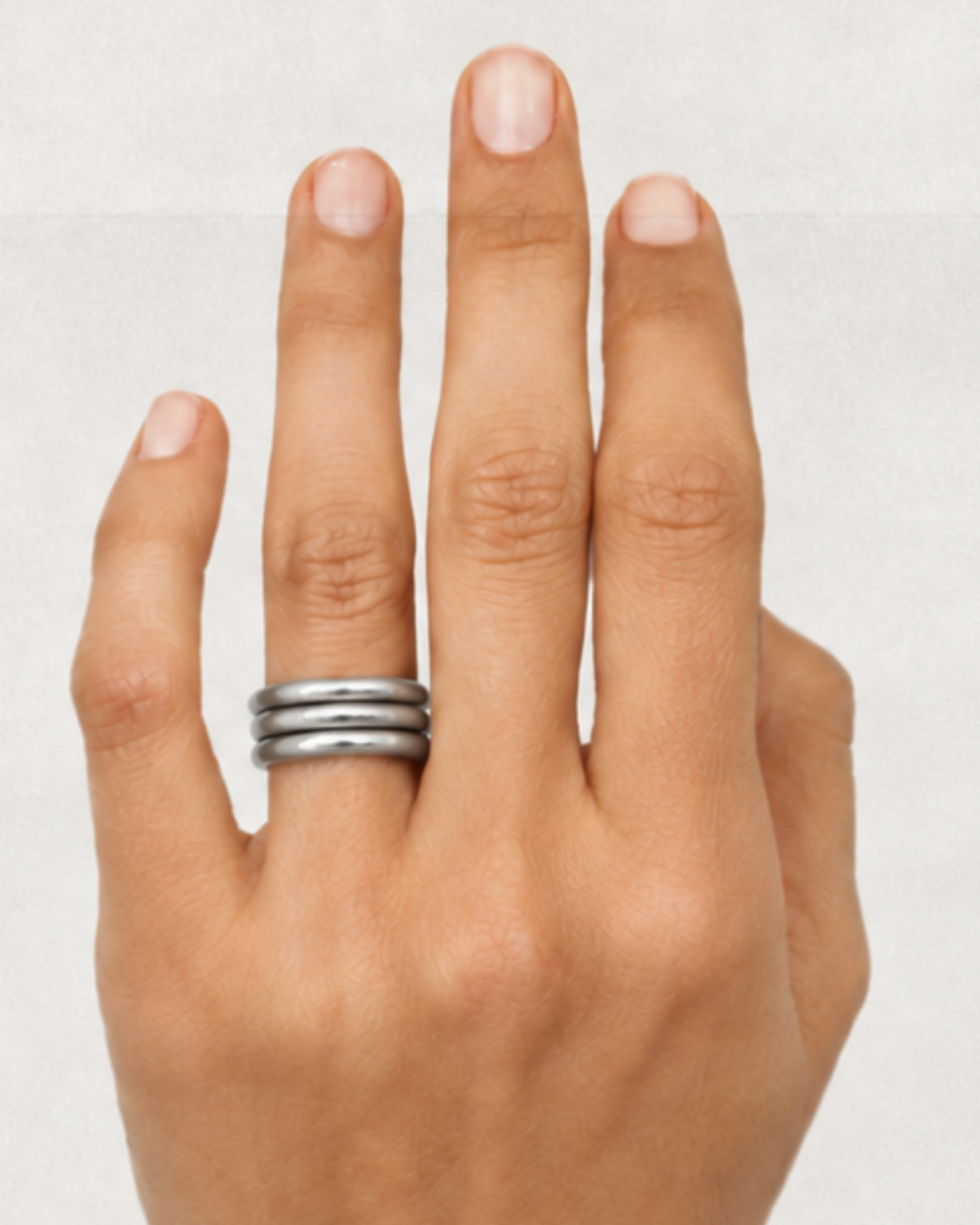 Hand wearing three stacked silver-toned rings on the middle finger against a light background
