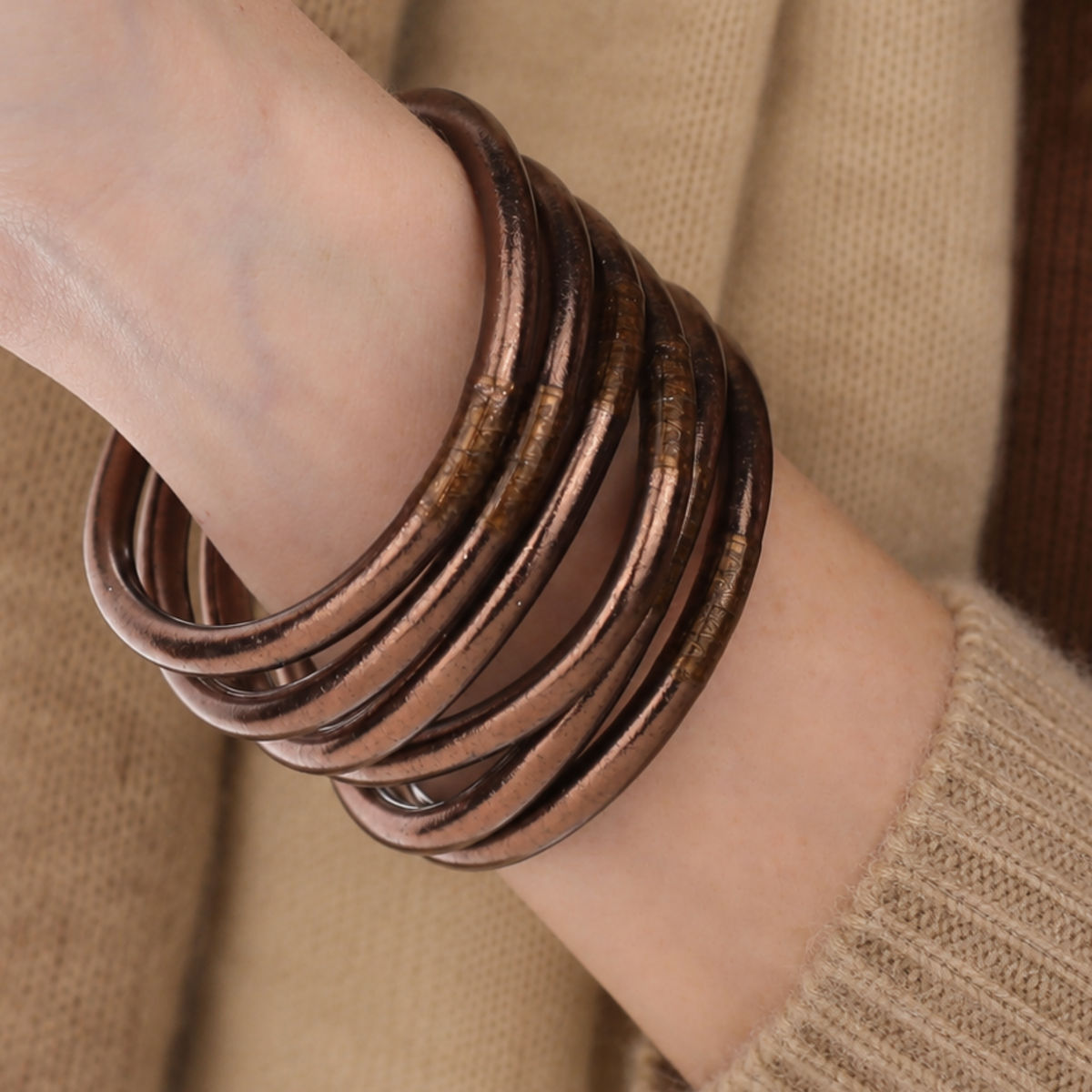 A close-up of a person's wrist wearing a stack of meteorite all weather bangles over a beige knit sweater.