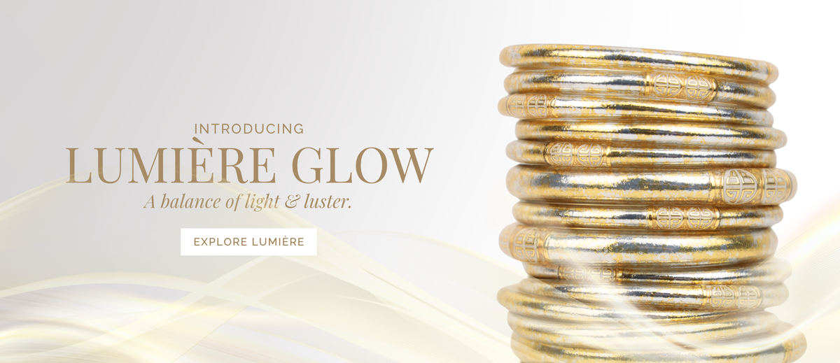 Stack of gold bangle bracelets beside text reading Introducing Lumiere Glow and A balance of light and luster on a soft cream background