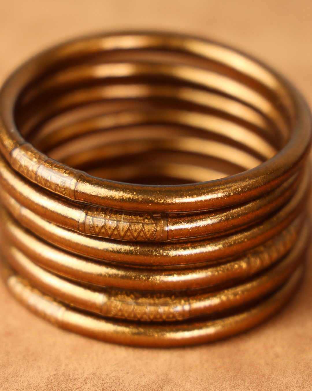 A close-up of a stack of copper metallic bangles on a warm tan background.